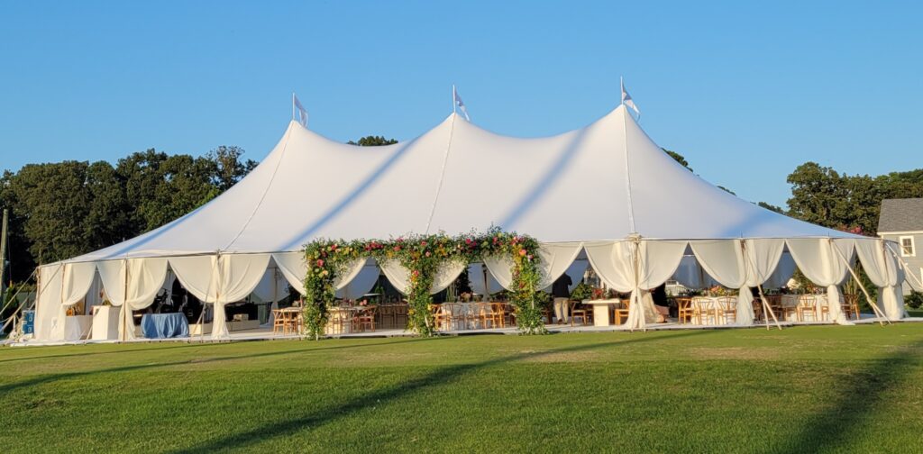 white tent set up on lawn with floral archways draped around entrance.