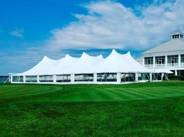 60x120 high peak pole tent with clear sidewalls set up on lawn with blue sky above.