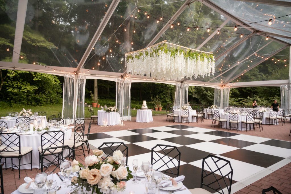 clear top frame tent set up on brick patio, with black and white dance floor and white floral suspended chandelier