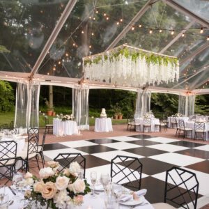 clear top tent with black and white dance floor and suspended floral chandelier set up for wedding over a patio