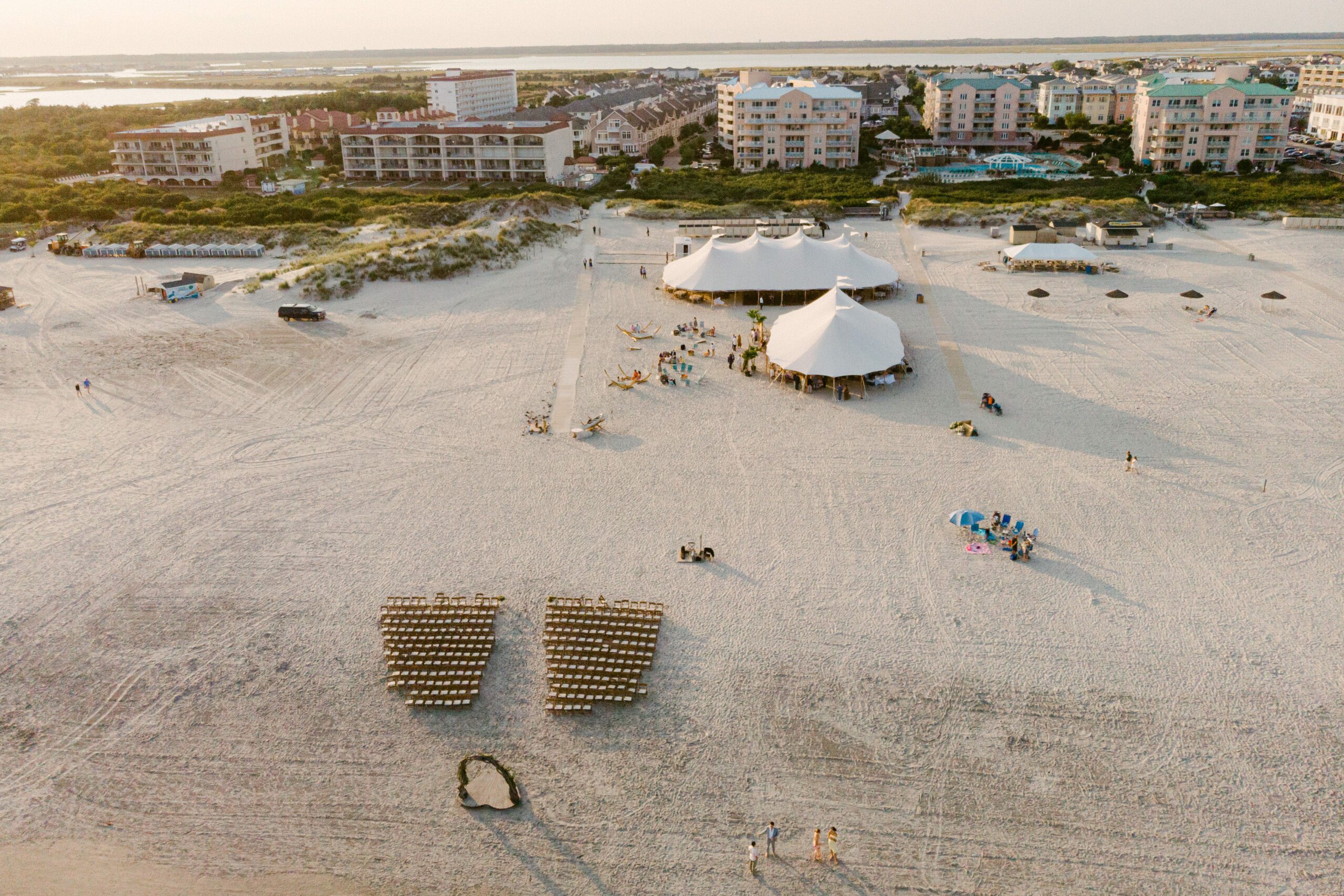 drone view of large white tents set up on beach, with chairs in rows for wedding ceremony