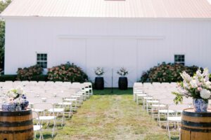 white wedding ceremony chairs set up in rows with wine barrel backdrop