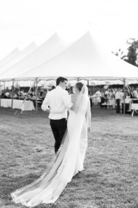 black and white photo of bride and groom walking towards wedding tent