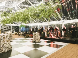Cocktail tables on a black and white dance floor with galaxy lighting and greenery hanging from the tent ceiling