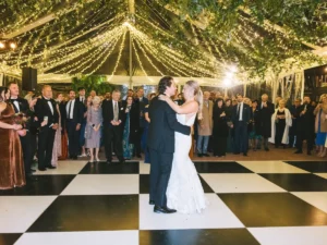 Bride and Groom doing their first dance on a black and white dance floor under a cleartop tent with galaxy lighting and greenery from the ceiling
