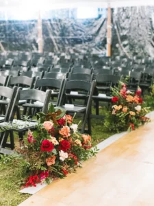 Black folding chairs lining a walkway for ceremony with red and pink florals
