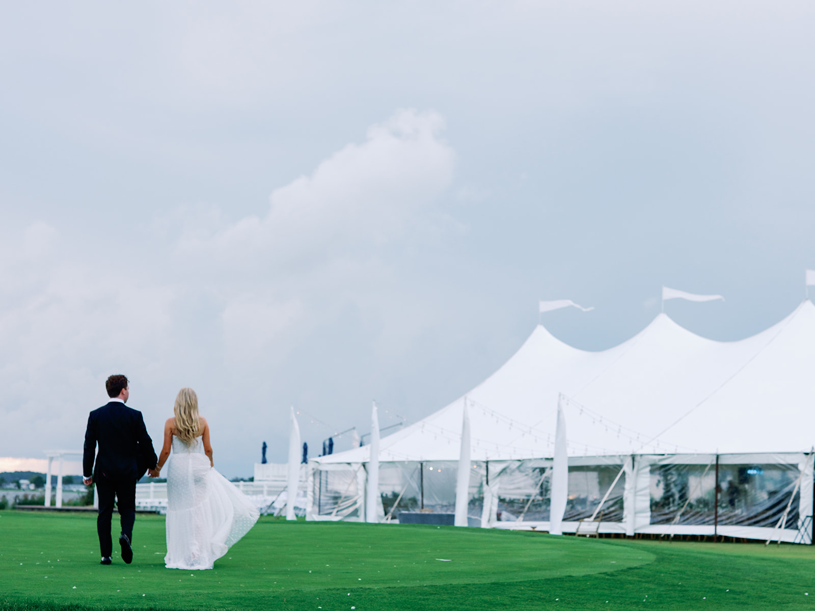 bride and groom walking towards sailcloth wedding tent on lawn