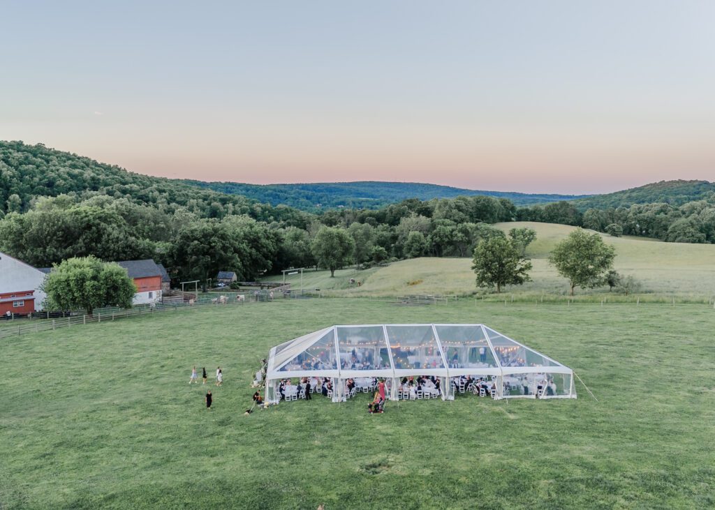 drone view of clear top wedding tent, on green rolling hills