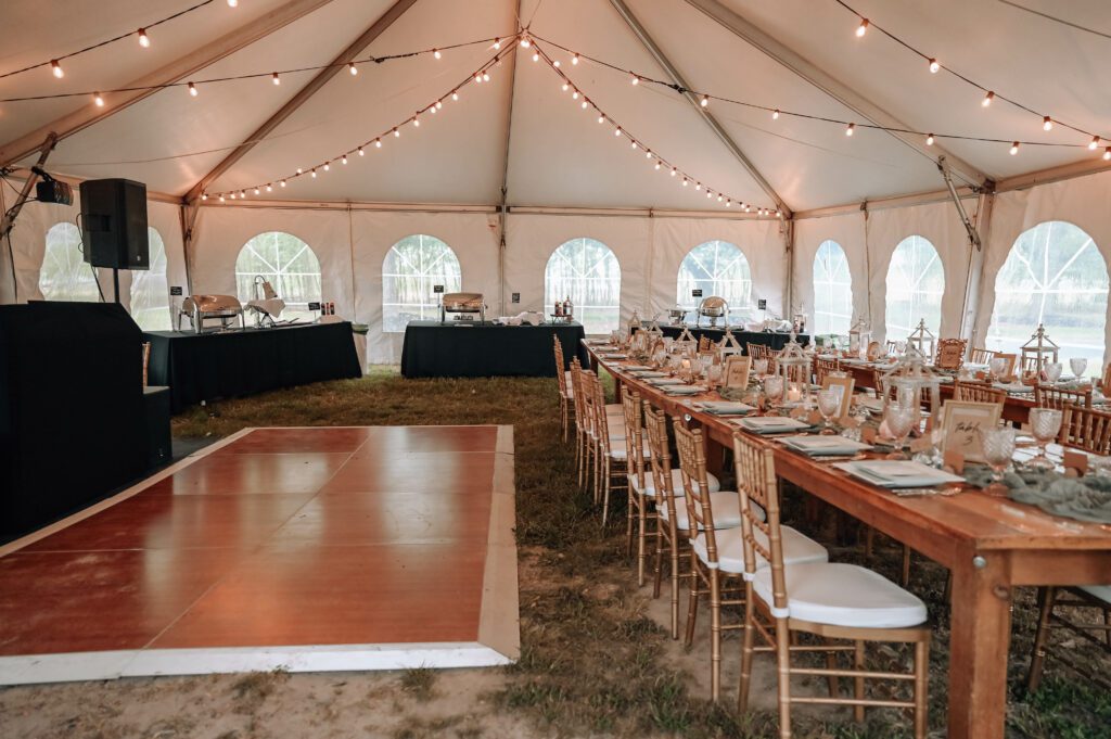 white tent set up for wedding reception with farmhouse tables and chiavari chairs