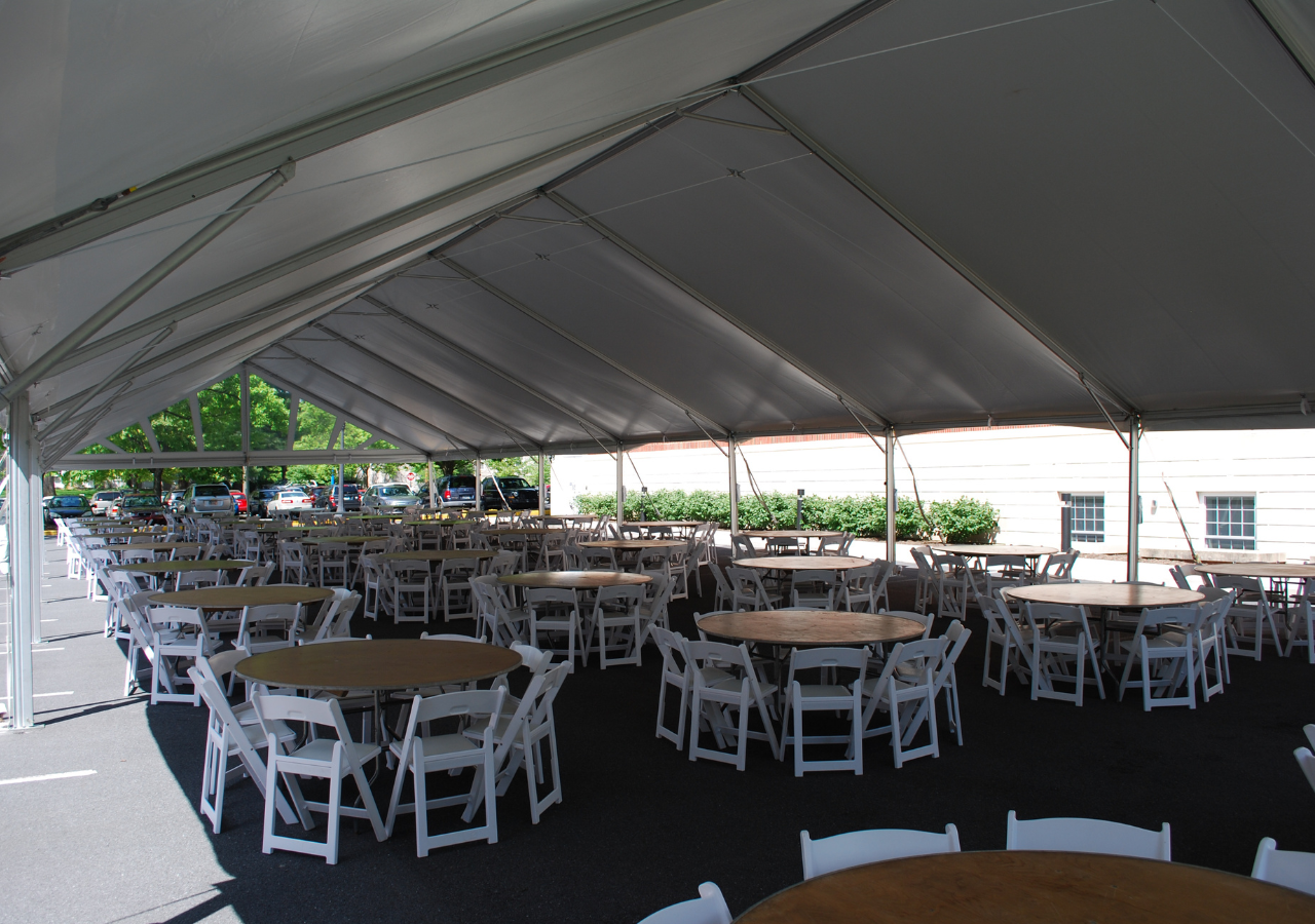 Round tables and white padded folding chairs under a frame tent for an event