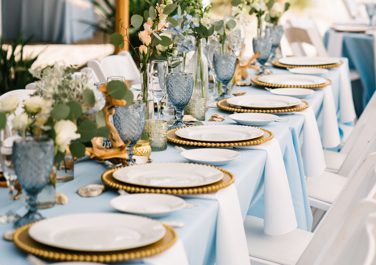 Tabletop items such as goblets, dinner plates, chargers on a blue linen