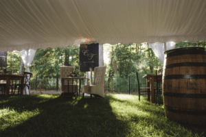 Inside tent view of sweetheart table with white tufted chairs and a wine barrel