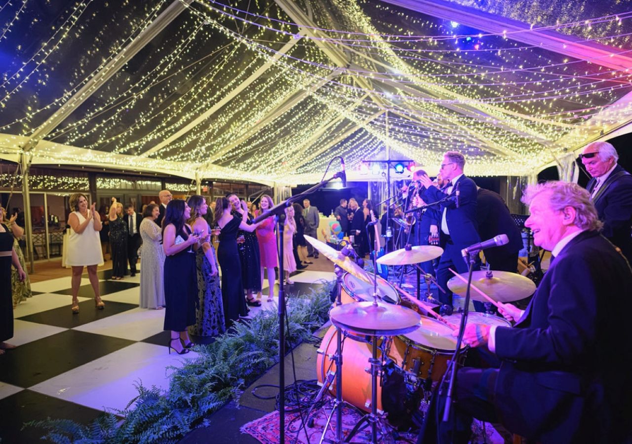 A cleartop tent with string lighting over a band with a black and white dance floor