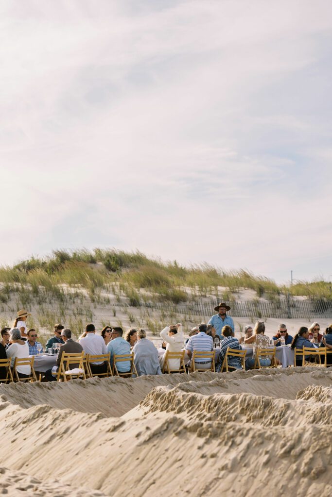 guests seated for outdoor dining at long table on sandy beach