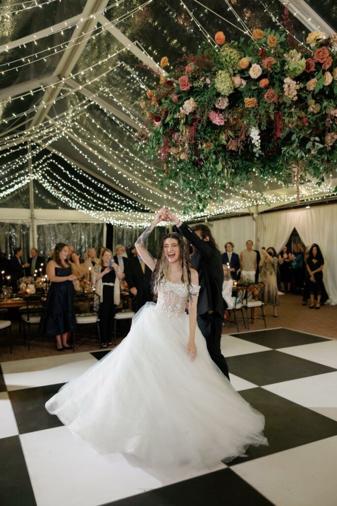 bride and groom dancing on black and white dance floor under wedding tent draped with twinkle lighting