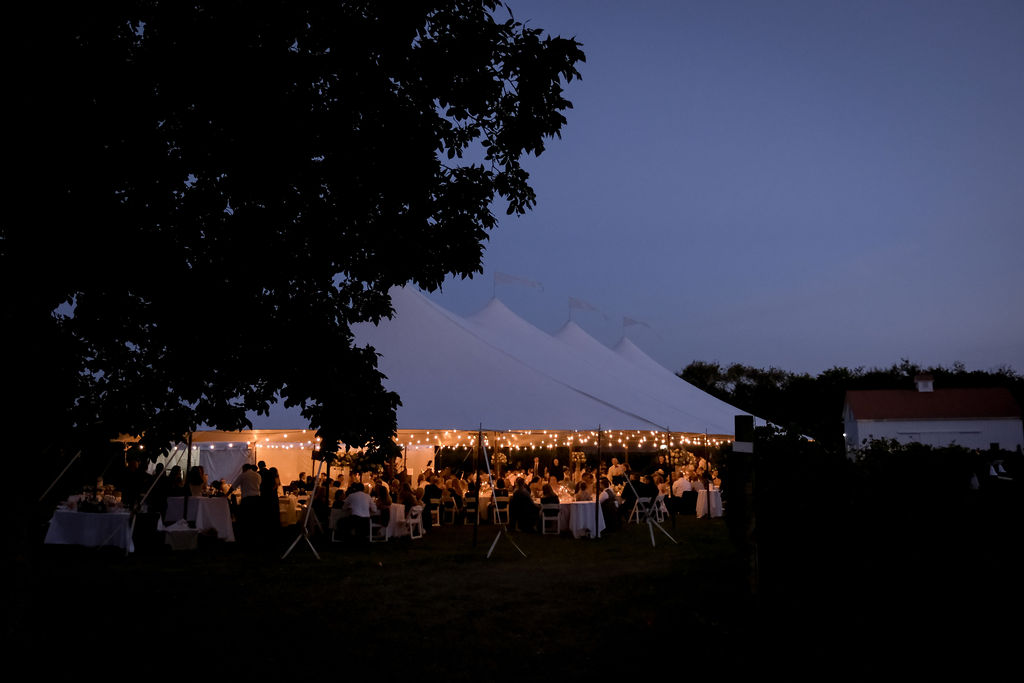 white sailcloth wedding tent with lighting glowing in the evening dusk sky.