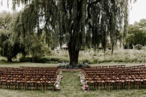 chairs set up for outdoor wedding ceremony in front of willow tree