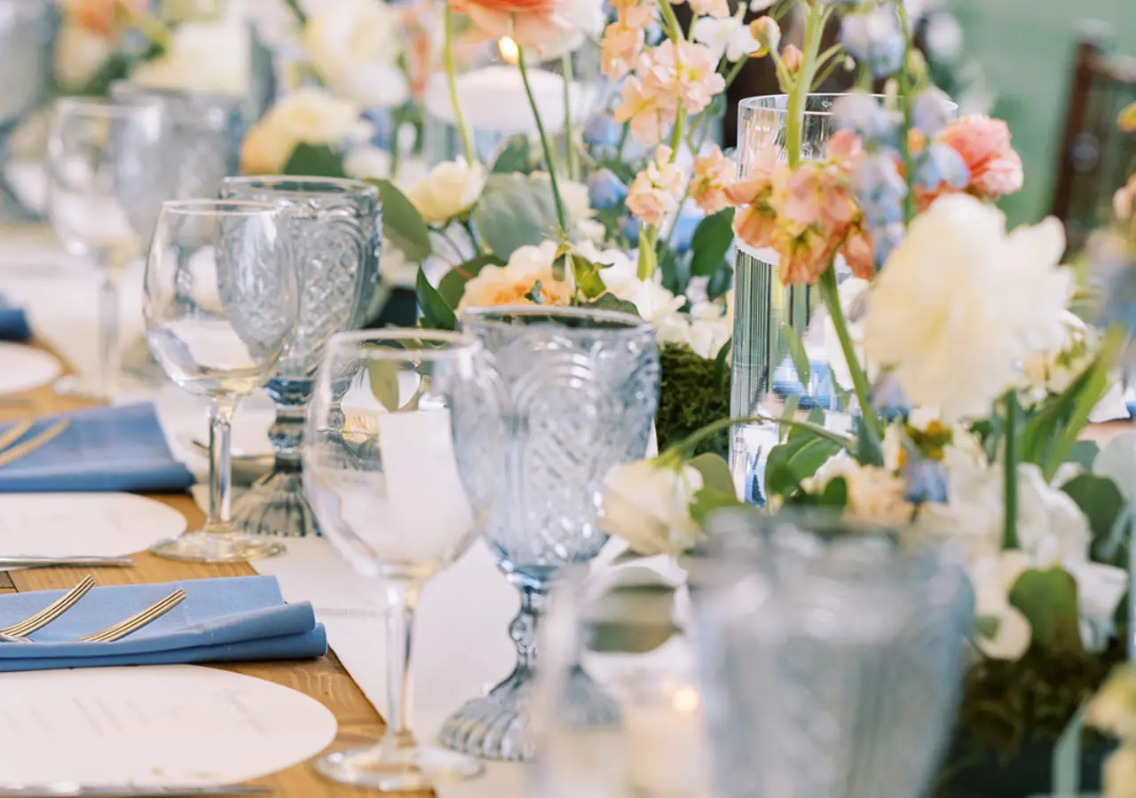 Up close view of a reception table with blue goblets, bouncy florals and tablesettings