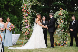 bride and groom at alter with floral back drop during outdoor wedding ceremony