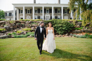 bride and groom, walking on grass in front of stone estate