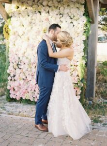 bride and groom standing in front of floral wall at wedding