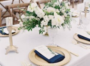 tablescape with white linens, gold charger plates, and navy blue napkins