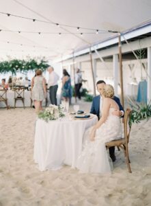 bride and groom at sweet heart table, under a sailcloth wedding tent for beach wedding on the sand