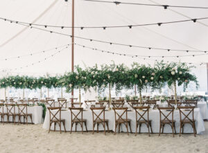 sailcloth tent with lighting wooden crossback chairs set up on sandy beach