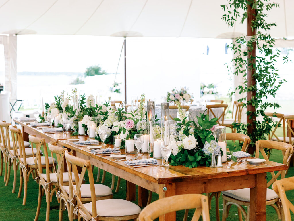 wooden farmhouse tables set up for guest seating under a wedding tent