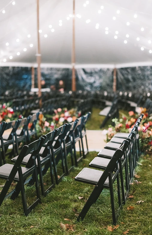 black chairs set up in rows under white tent for wedding ceremony